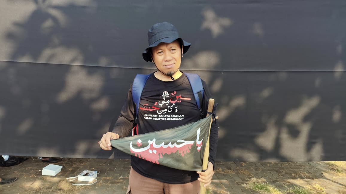 Darmaaji Lumintang membawa tongkat, bendera al-Husain dan ransel saat menyelesaikan perjalanan kaki sekitar 38 kilometer dari Kudus menuju Gedung Haji Jepara untuk mengikuti peringatan Arbain Imam Husain a.s., Selasa (4/8/2026).